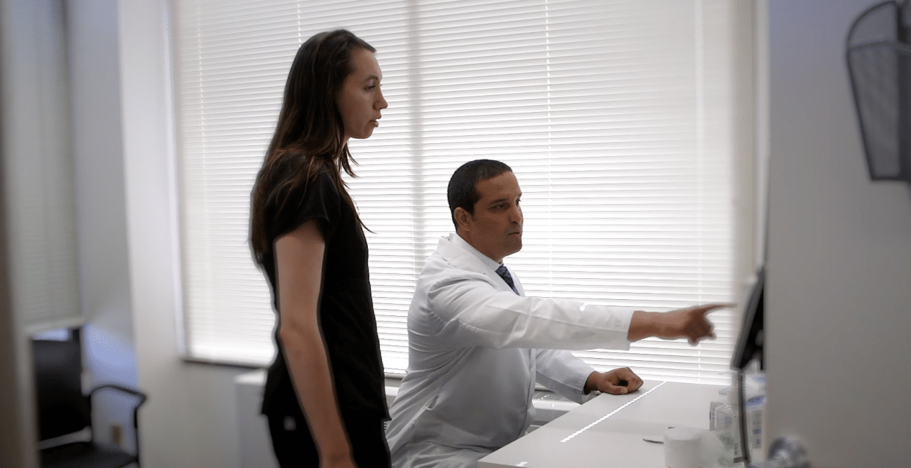 Screenshot 2026-05-22 at 24300 PM - Foundation Digital Media | Premier Video Production Services Male doctor in a white coat explains something on a computer screen to a standing female patient in a bright office setting.