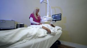Healthcare professional in pink scrubs adjusts a medical imaging device over a patient lying in a hospital bed, preparing a scan.